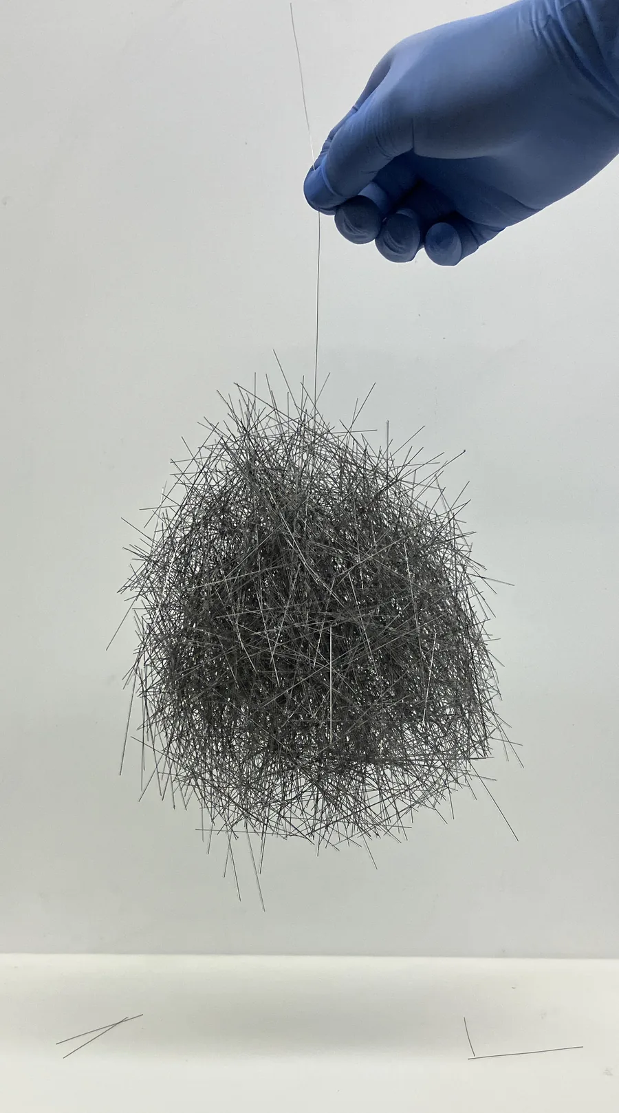 A ball of tangled thin rods hanging from a single rod held in a gloved hand.